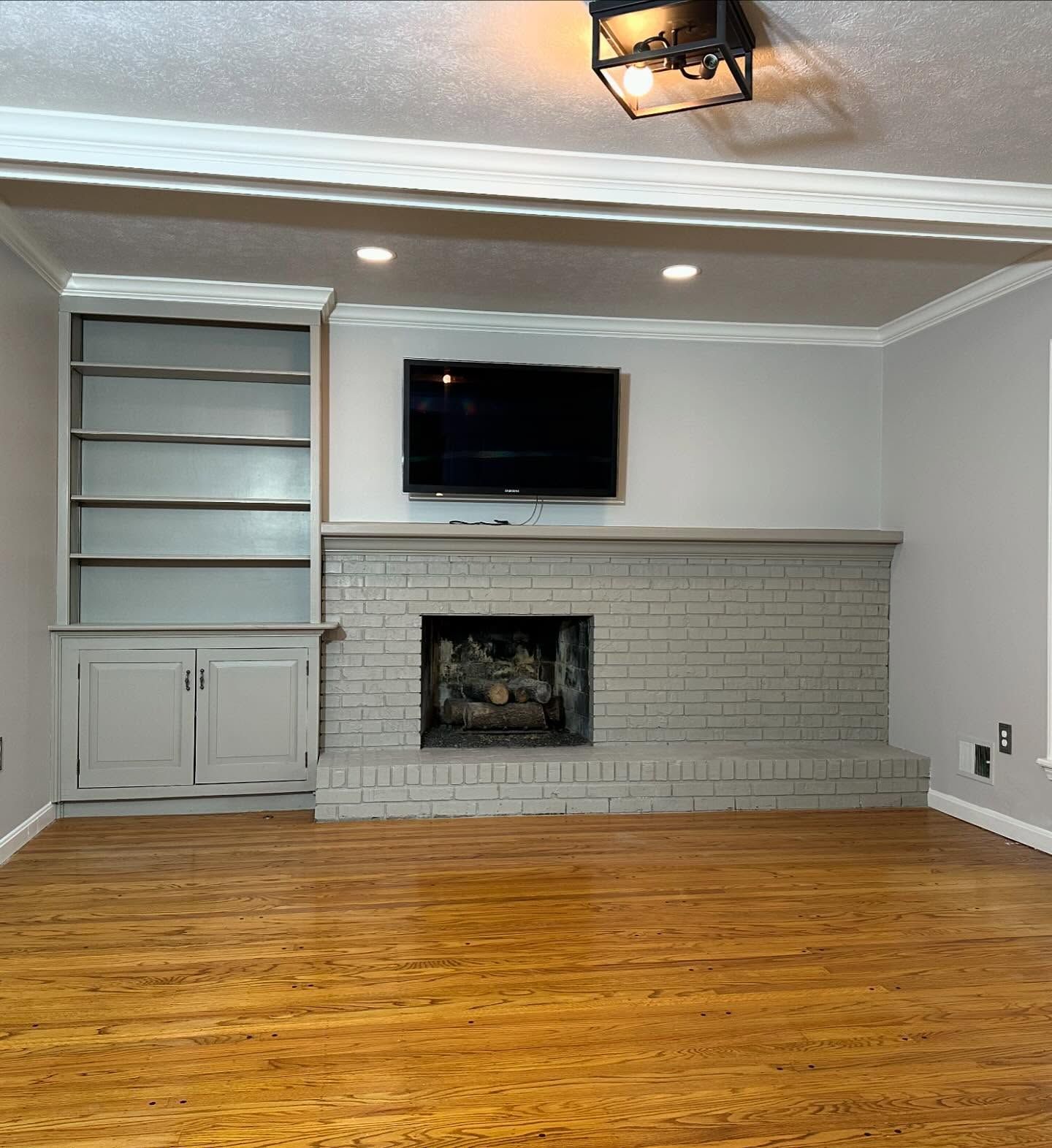 Living room with gray brick fireplace, built-in shelves, wall-mounted TV, and hardwood floor. Living room with gray brick fireplace, built-in shelves, wall-mounted TV, and hardwood floor.