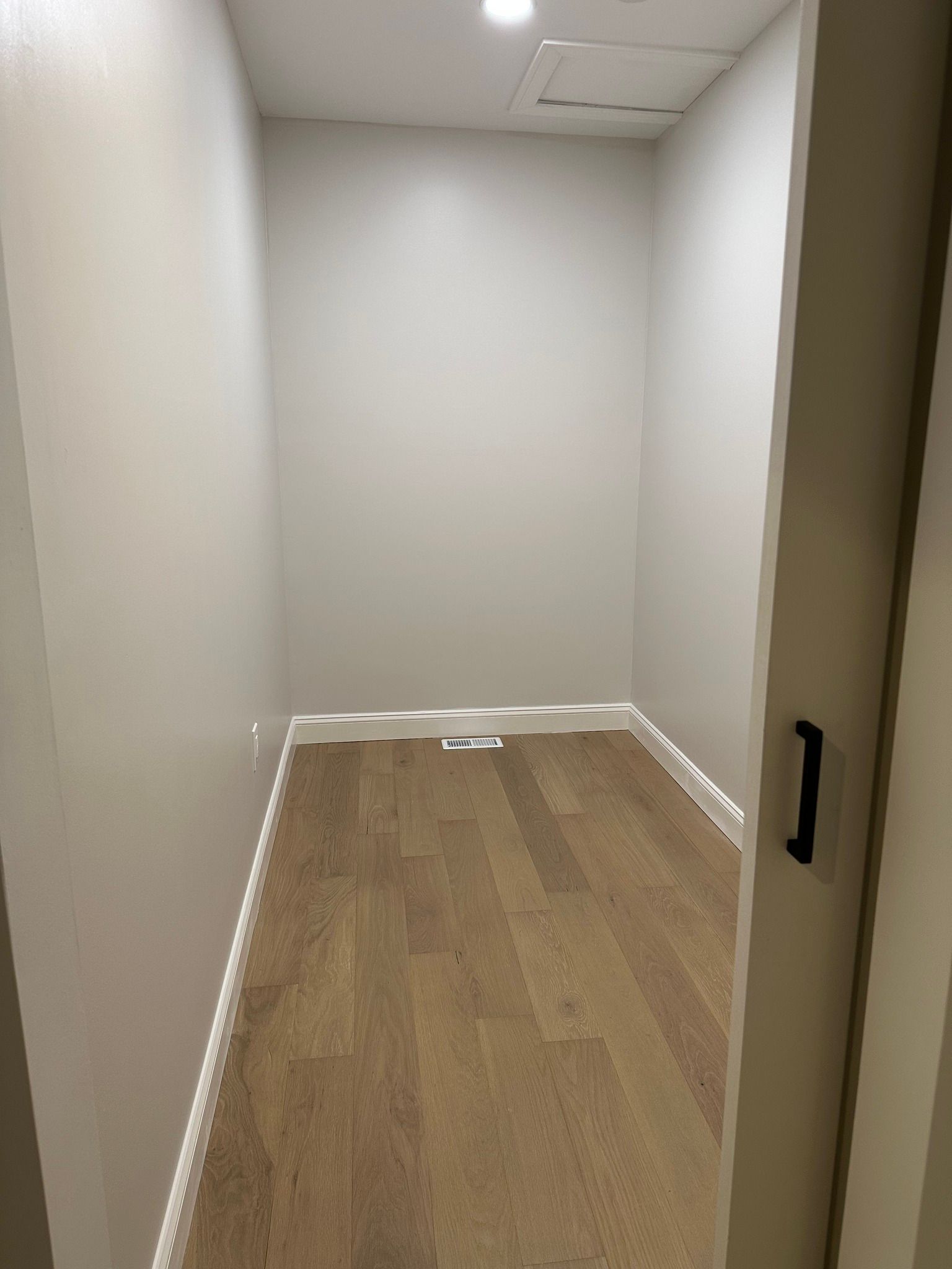 Empty narrow hallway with white walls, wood floor, and a partially open door. Empty narrow hallway with white walls, wood floor, and a partially open door.