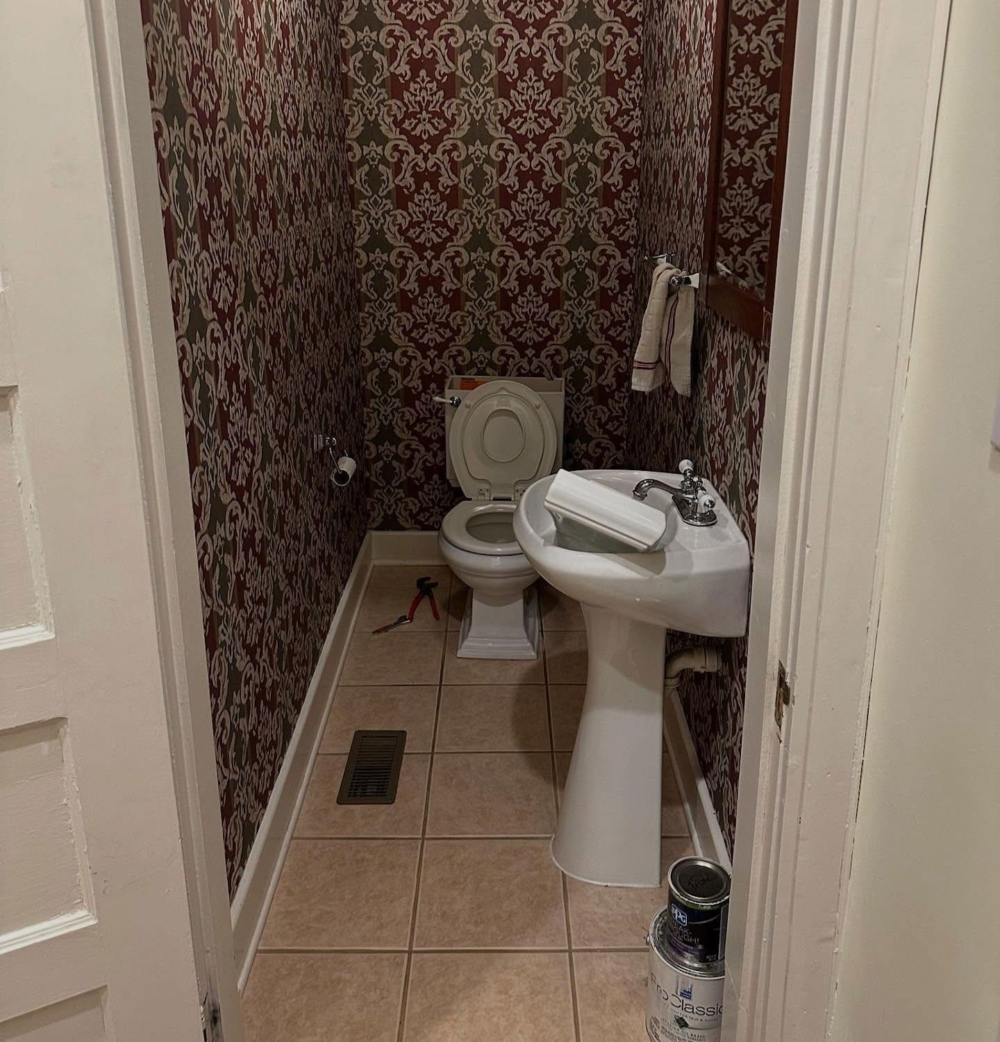 Small narrow bathroom with toilet, pedestal sink, patterned wallpaper, and tiled floor. Small narrow bathroom with toilet, pedestal sink, patterned wallpaper, and tiled floor.