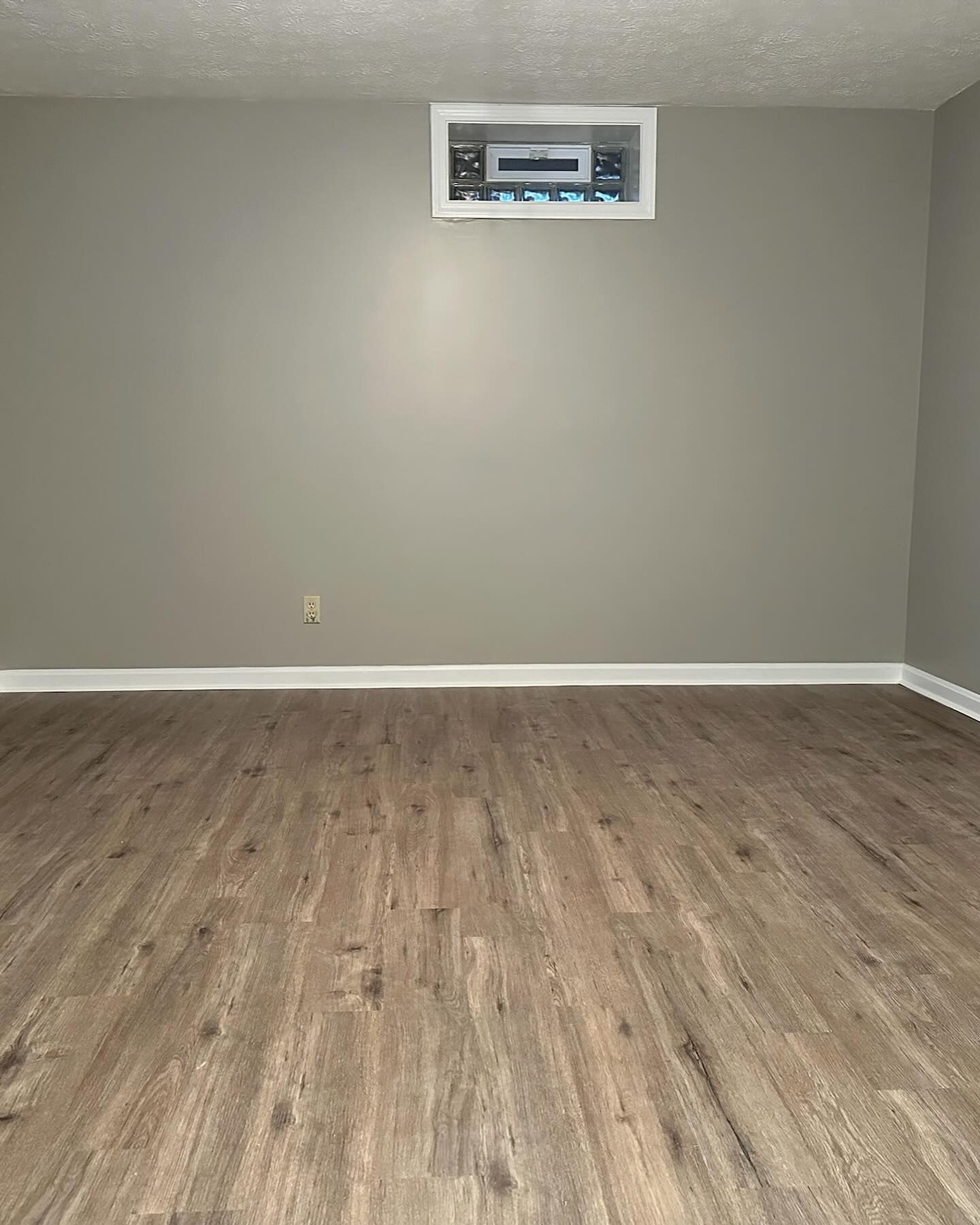 Empty room with gray walls, wood flooring, and a small wall vent near the ceiling. Empty room with gray walls, wood flooring, and a small wall vent near the ceiling.