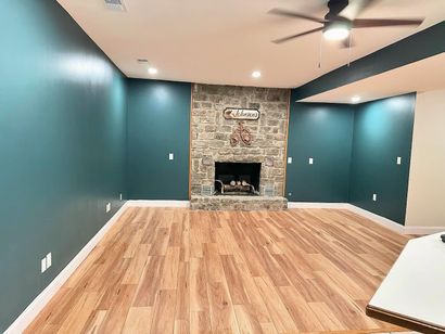 Empty living room with teal walls, wood floors, and a stone fireplace at the far end.