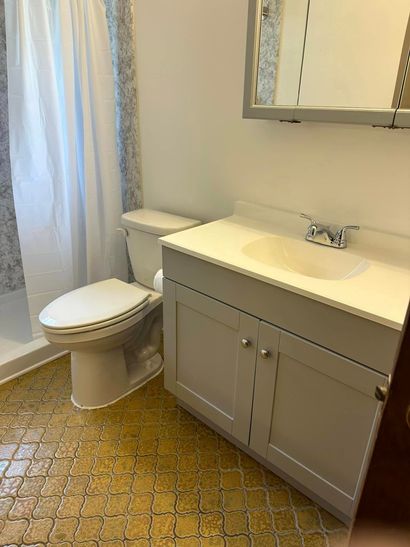 Bathroom with gray vanity, white sink, toilet, mirror, and shower curtain on a patterned floor.
