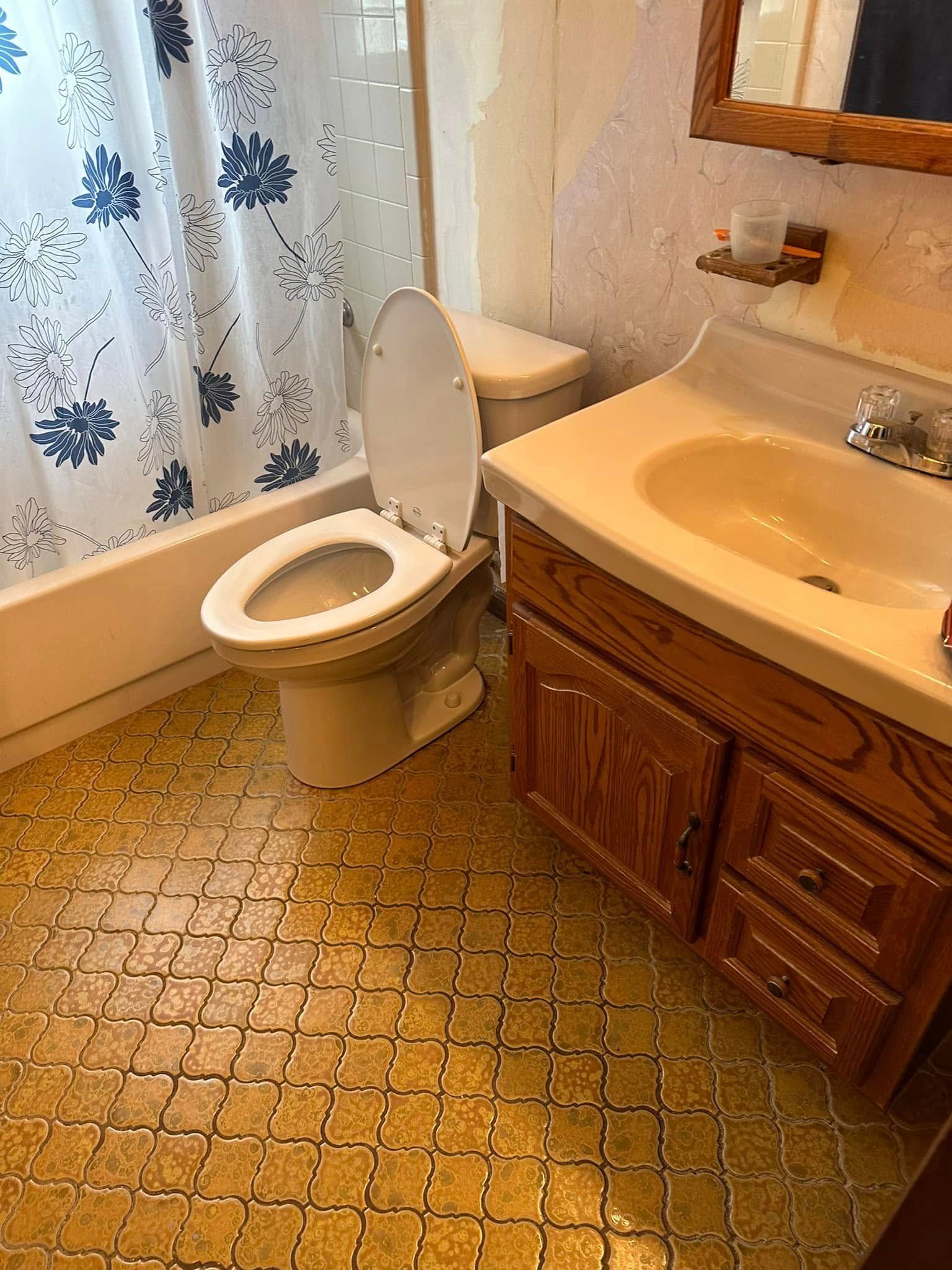 Small bathroom with open toilet, sink vanity, bathtub, and floral shower curtain. Small bathroom with open toilet, sink vanity, bathtub, and floral shower curtain.