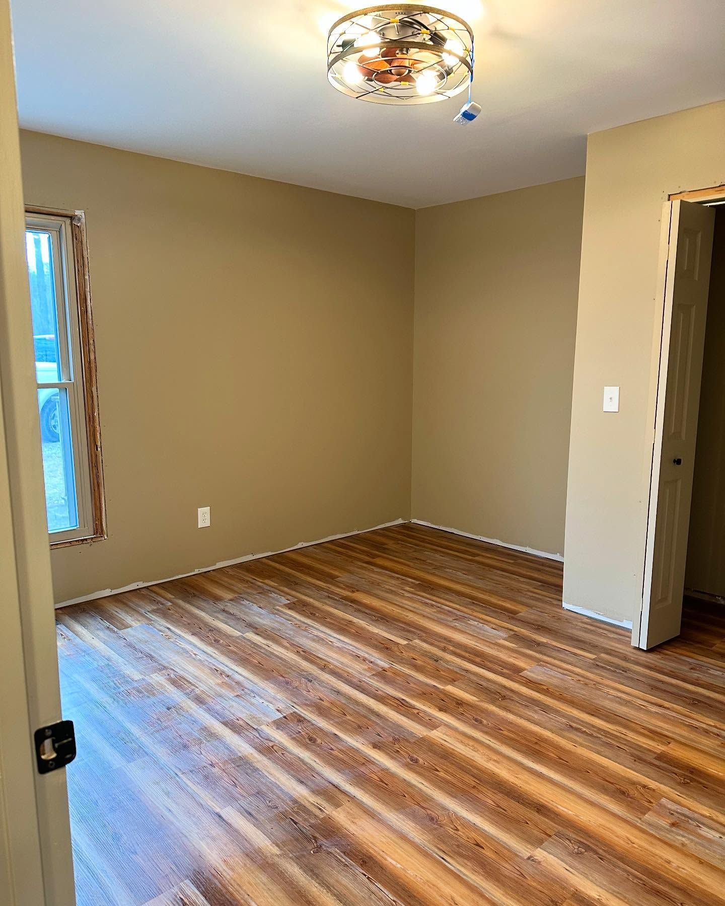 Empty beige room with wood-look floor, ceiling light fixture, and open doorway. Empty beige room with wood-look floor, ceiling light fixture, and open doorway.