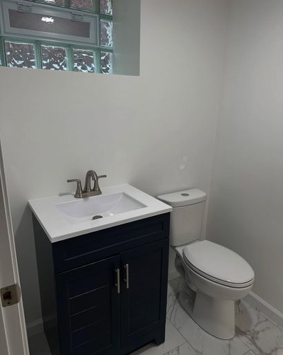 Small bathroom with white vanity, black cabinet, toilet, and window above the sink.
