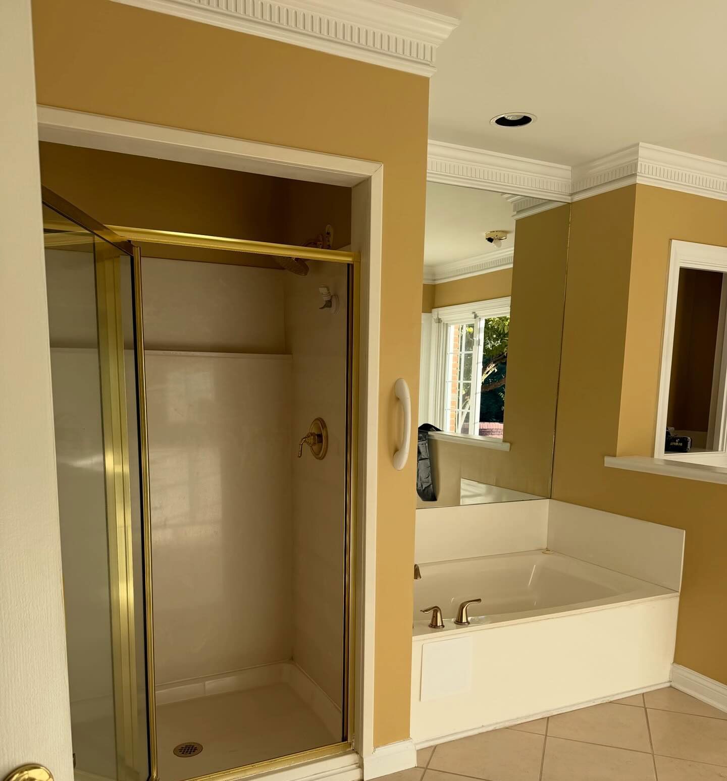 Bathroom with gold-framed shower stall, white tub, beige walls, and mirror by the sink. Bathroom with gold-framed shower stall, white tub, beige walls, and mirror by the sink.