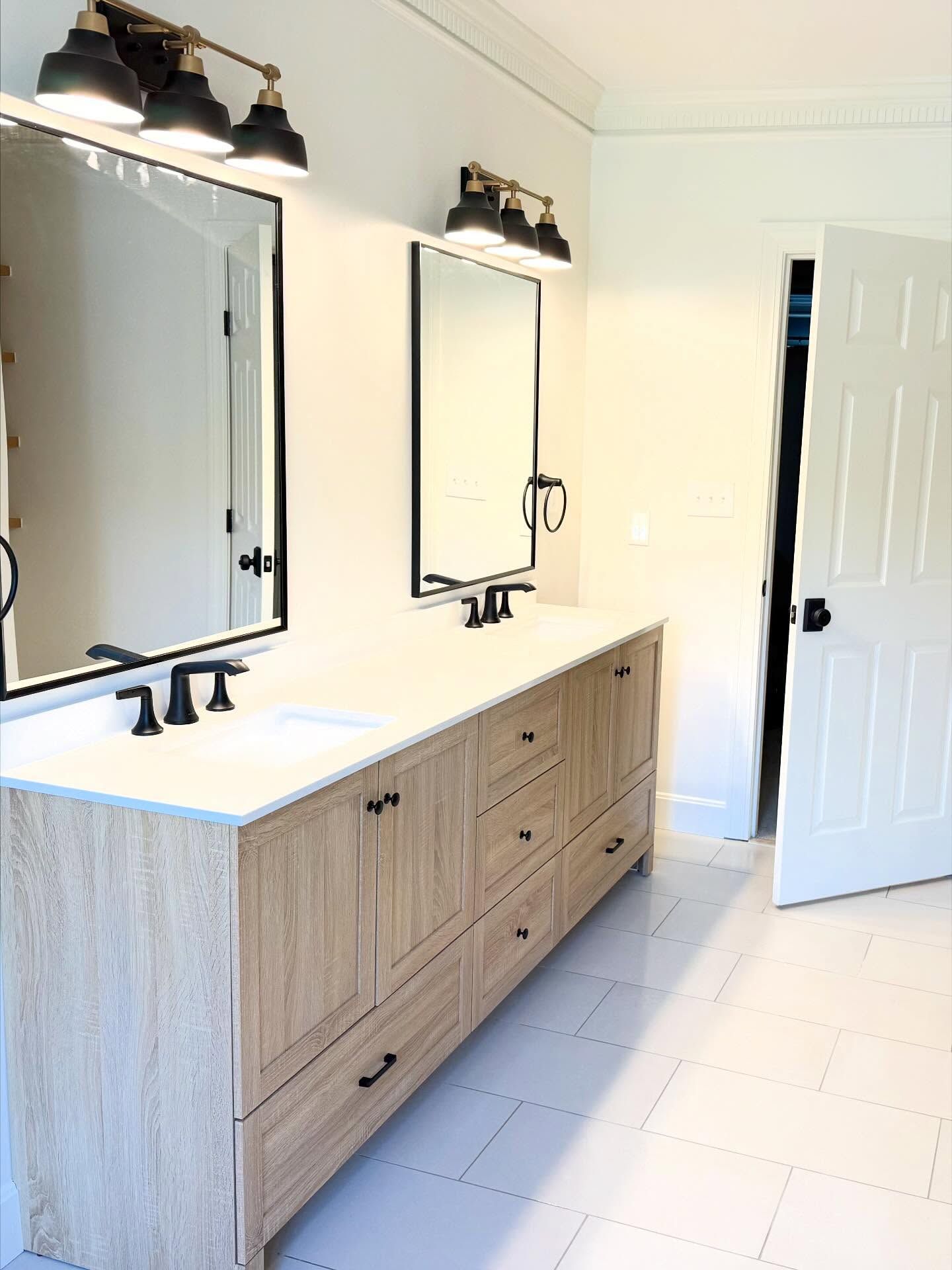 Modern bathroom with double sinks, wood vanity, large mirrors, black sconces, and white tile floor Modern bathroom with double sinks, wood vanity, large mirrors, black sconces, and white tile floor
