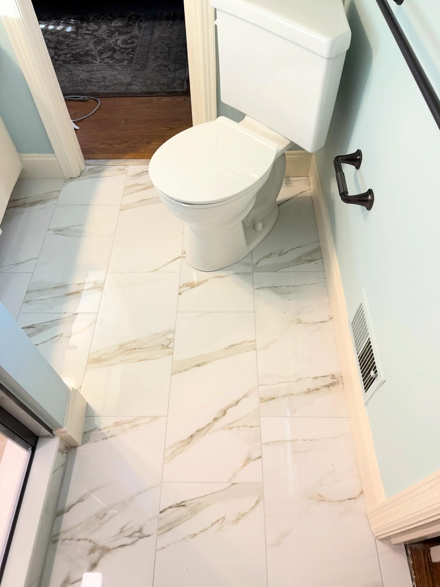 Small bathroom with white toilet, light tile floor, and a black wall-mounted toilet paper holder. Small bathroom with white toilet, light tile floor, and a black wall-mounted toilet paper holder.