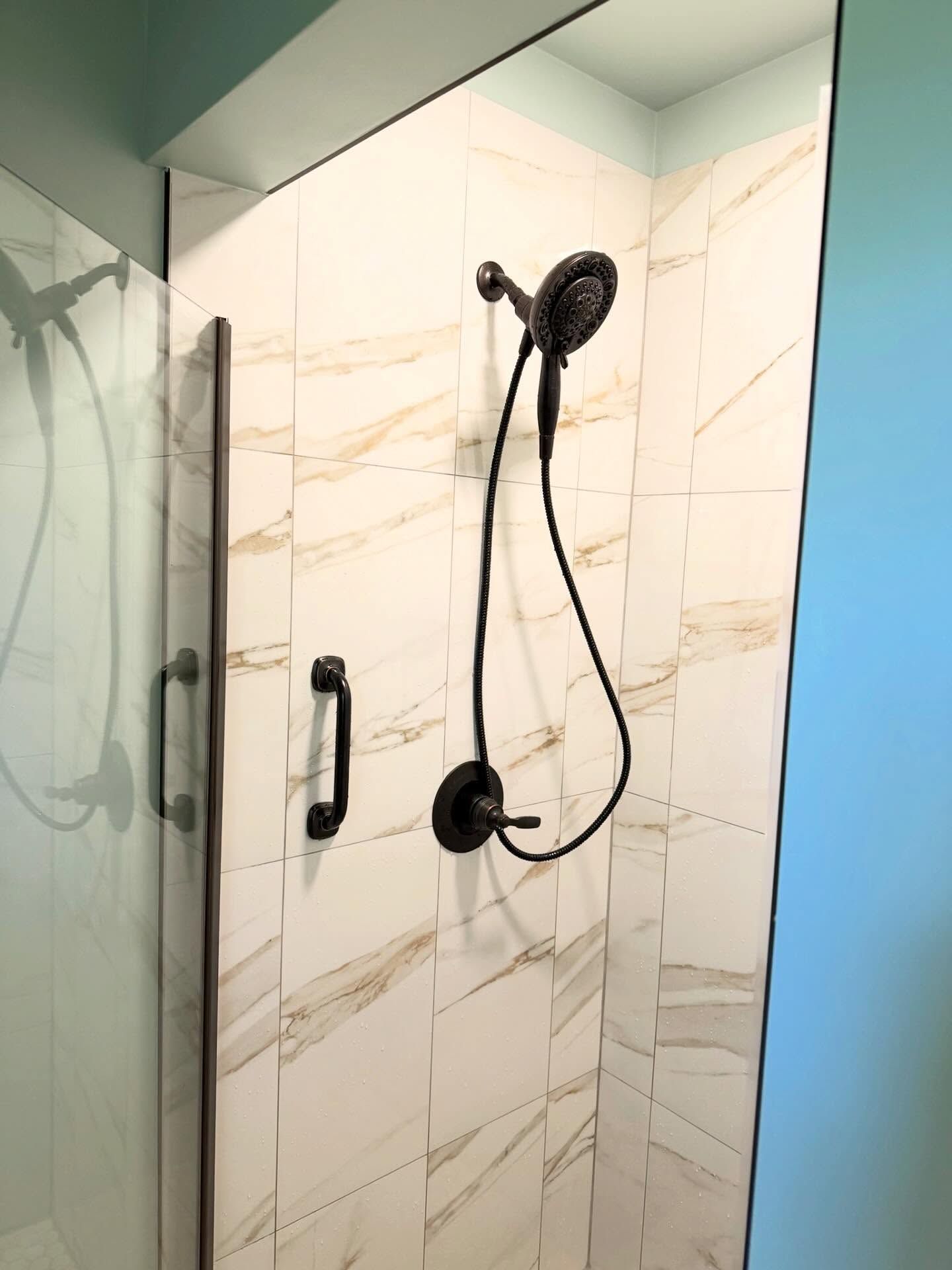 Modern shower with beige tile, glass door, and black handheld showerhead on a white marble wall Modern shower with beige tile, glass door, and black handheld showerhead on a white marble wall