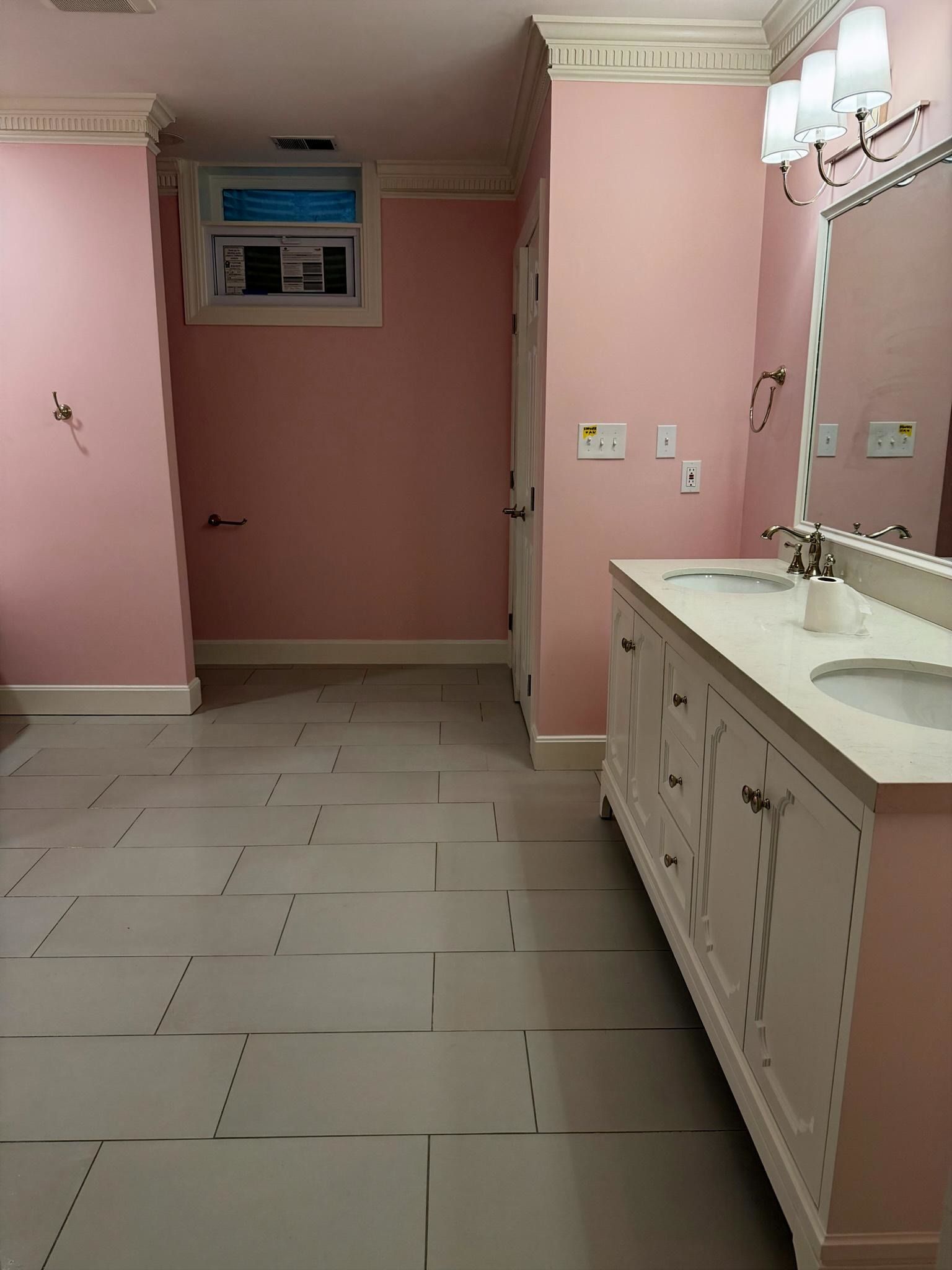 Pink bathroom with white tile floor, vanity, and mirror cabinets; doorway at the far end. Pink bathroom with white tile floor, vanity, and mirror cabinets; doorway at the far end.