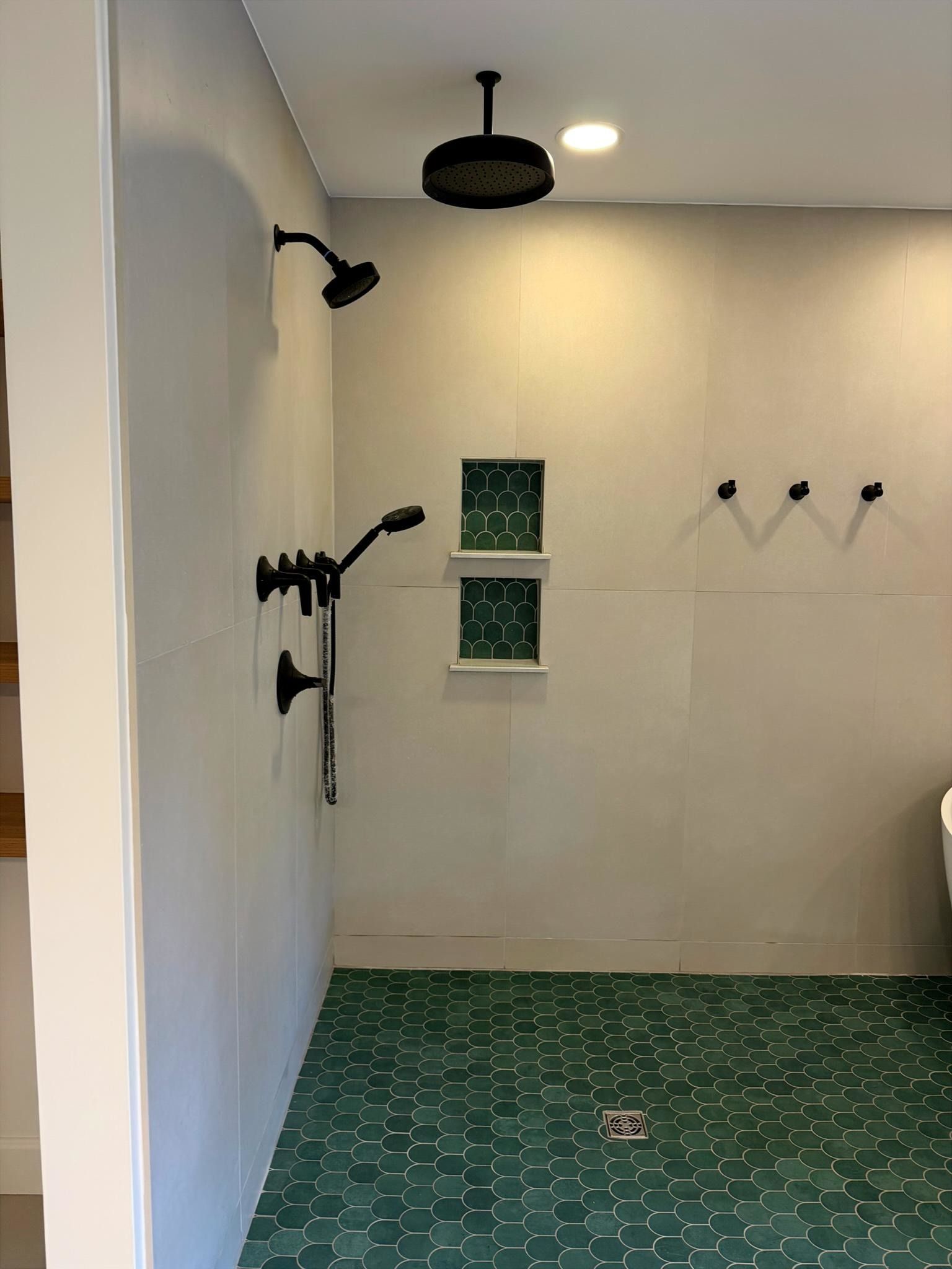 Empty shower stall with white walls, black fixtures, and green patterned tile floor and window accents Empty shower stall with white walls, black fixtures, and green patterned tile floor and window accents