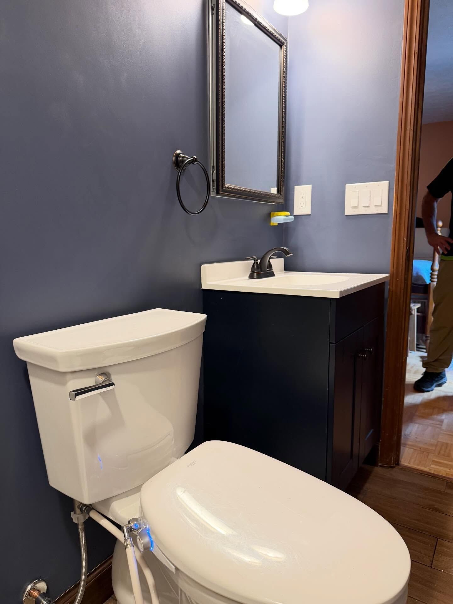 Small bathroom with white toilet, dark vanity, wall mirror, and navy blue walls. Small bathroom with white toilet, dark vanity, wall mirror, and navy blue walls.
