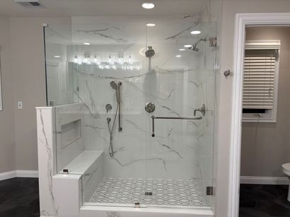 Modern bathroom with glass-enclosed marble shower, bench, and patterned tile floor