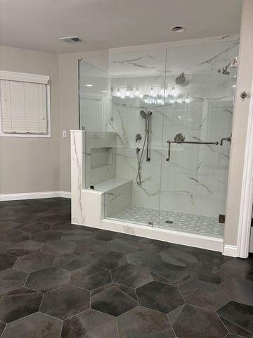 Modern bathroom with glass-enclosed shower, white marble tile, and dark hexagon floor tiles