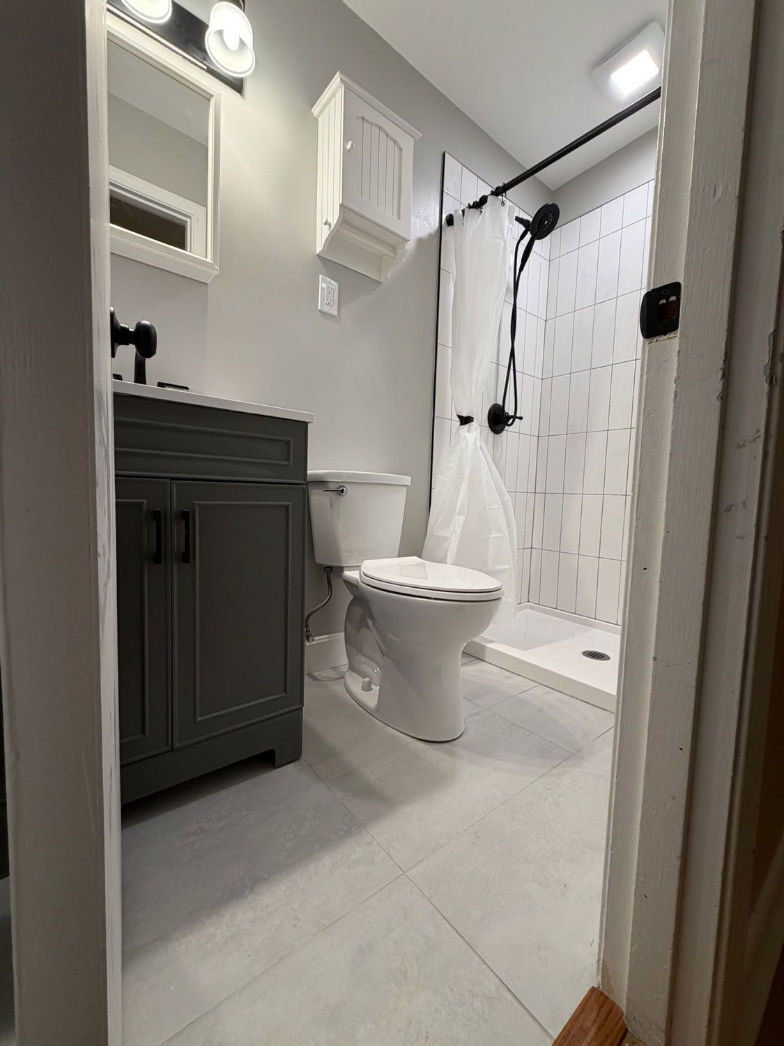 Small bathroom with vanity, toilet, and shower in gray and white tones.