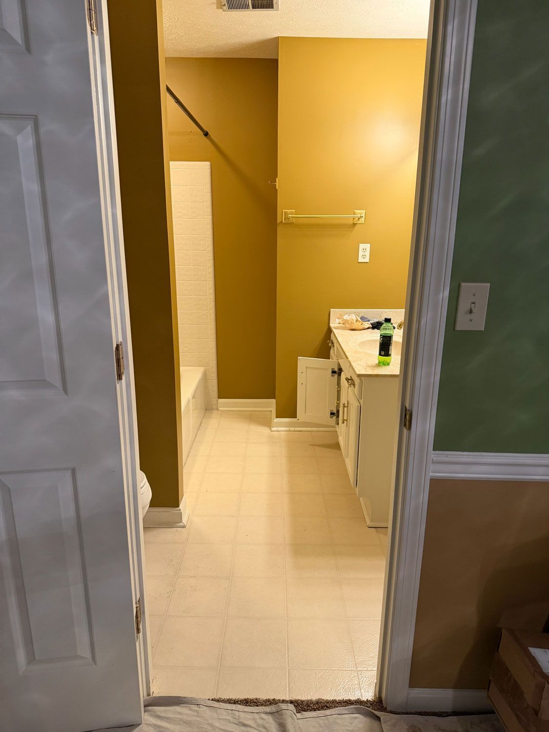 View through doorway into a small bathroom with mustard-yellow walls, white tile floor, and a sink on the right. View through doorway into a small bathroom with mustard-yellow walls, white tile floor, and a sink on the right.