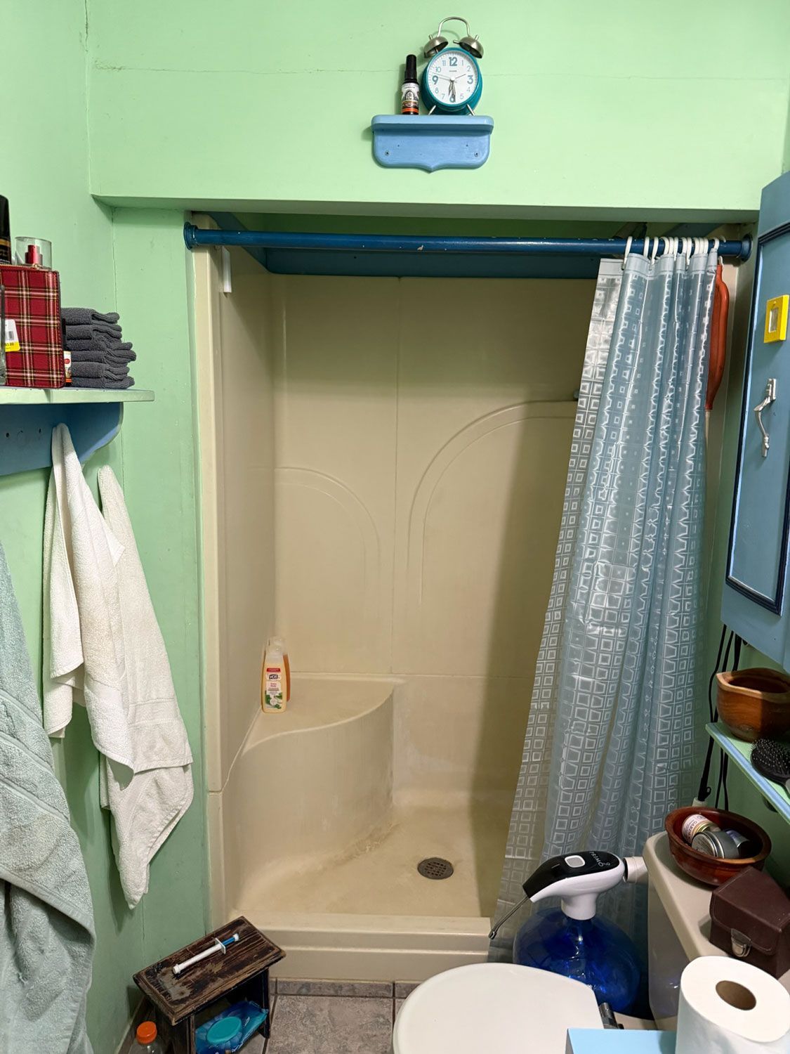 Small bathroom with a shower stall, blue trim, towels, and toiletries on shelves.