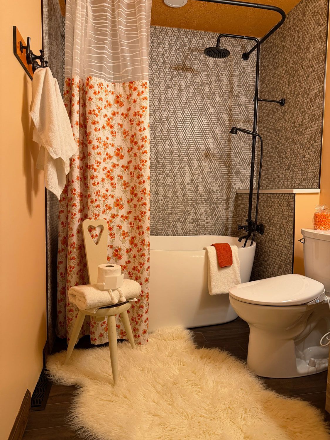 Cozy bathroom with orange walls, floral shower curtain, white toilet, vanity, and fluffy cream rug