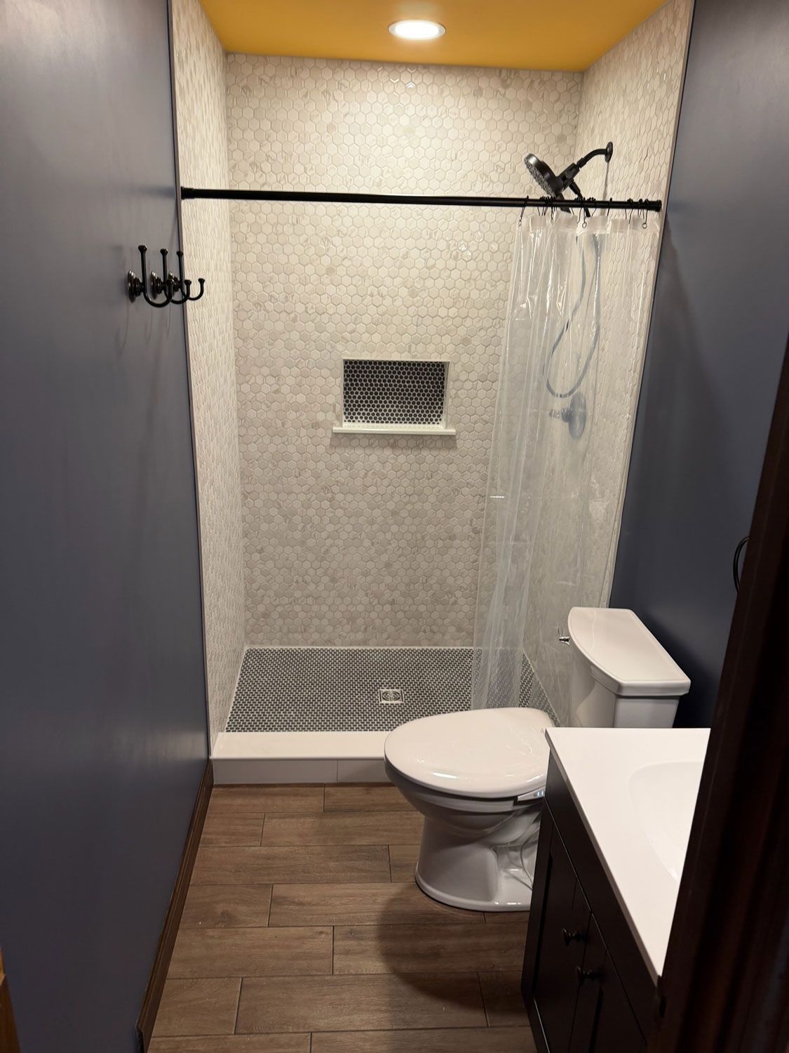Small modern bathroom with toilet, sink, shower, and gray textured walls.
