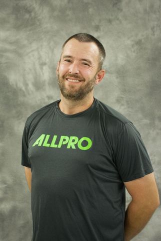 Smiling man in a black ALLPRO T-shirt standing against a gray backdrop