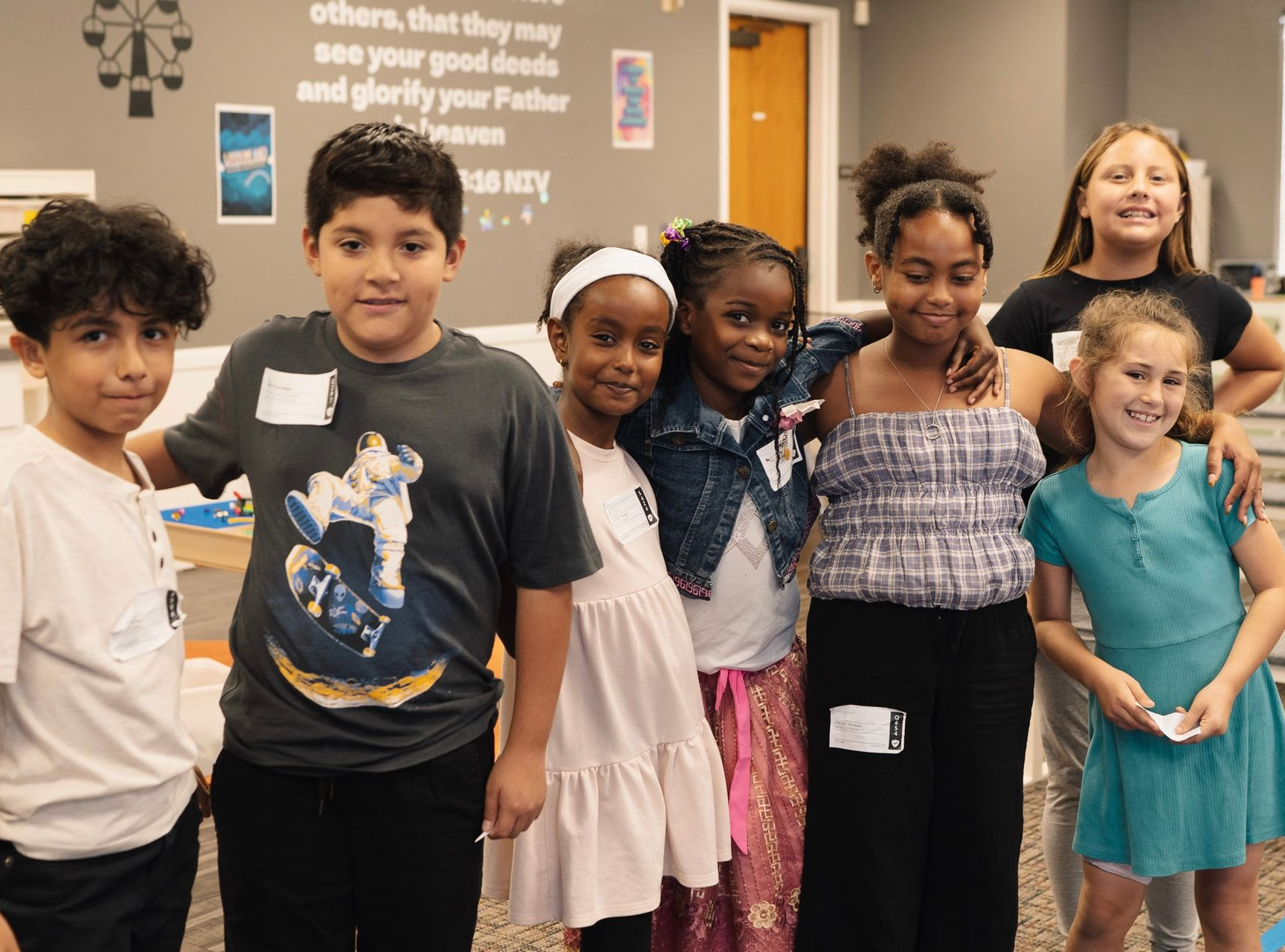 Children posing together indoors in a classroom, smiling and standing in a row