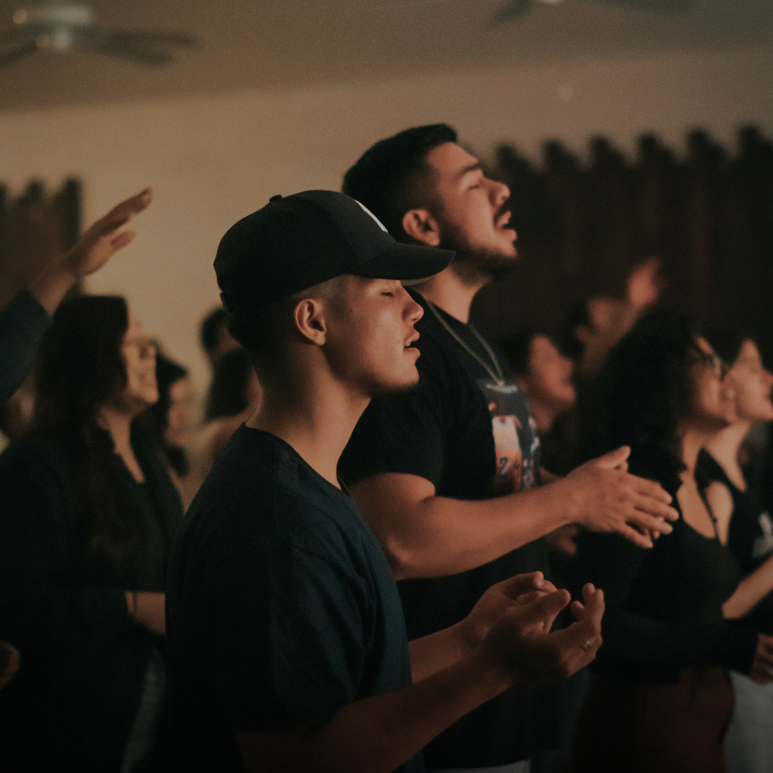 People in a warmly lit room with raised hands, singing and worshiping.