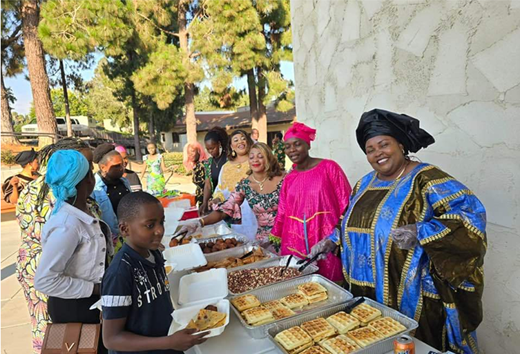 People serving food at an outdoor event, some wearing colorful African attire.