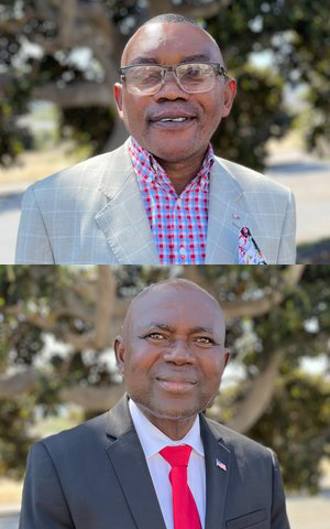 Two men in suits, smiling. One wears glasses, a plaid shirt, and a light-colored jacket. The other wears a black suit and red tie.