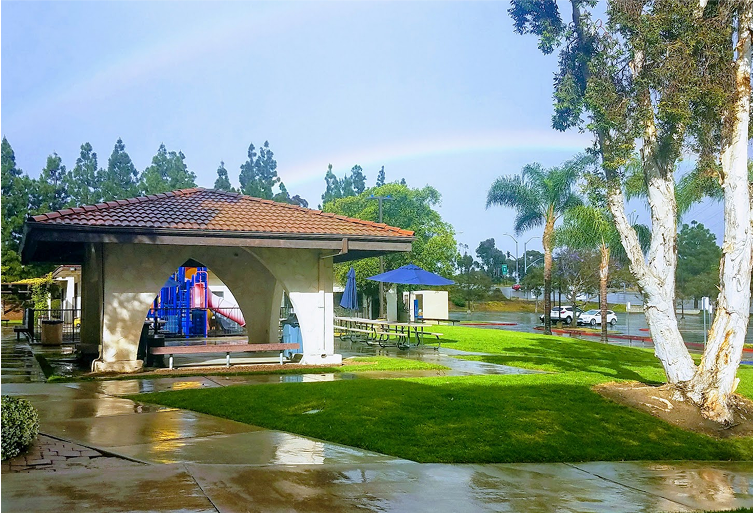 Park with gazebo and playground under a rainbow. Wet grass, clear sky. San Diego rainy day. 