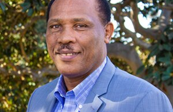 Man wearing a blue suit, smiling. Outdoor setting with trees visible.