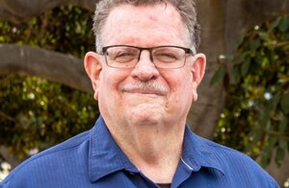 Man wearing glasses and a blue shirt, smiling outdoors.