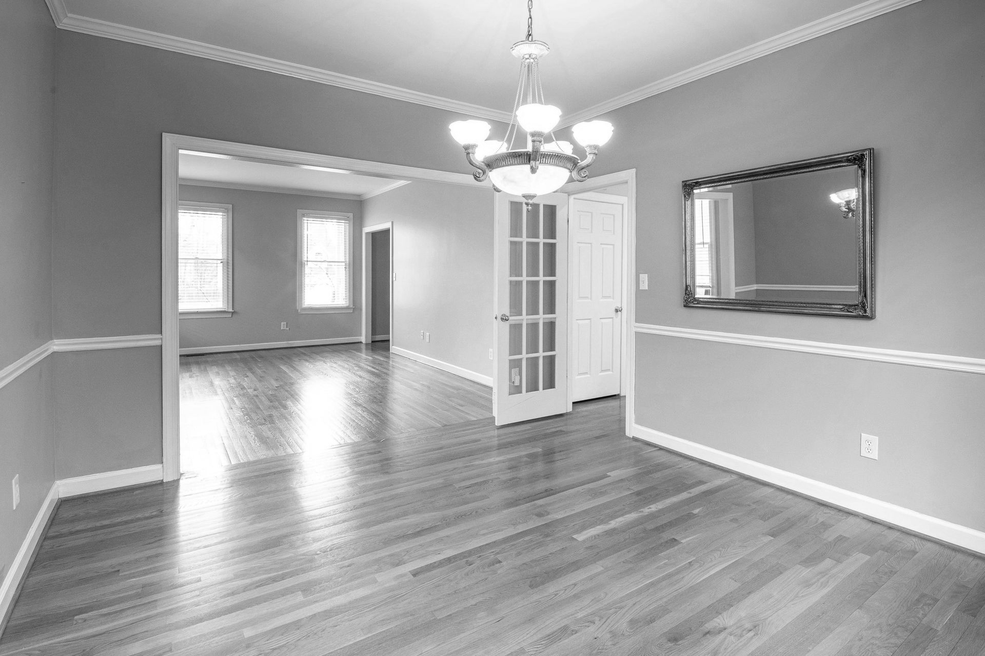 Empty dining room with hardwood floors, chandelier, and doorway to another room.