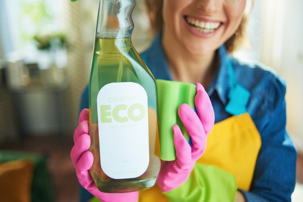A woman wearing pink gloves is holding a spray bottle and a cloth.