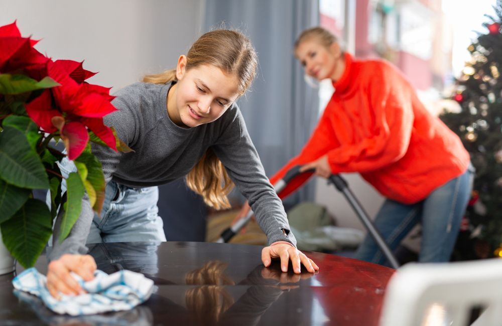 Two girls are cleaning a table in a living room.