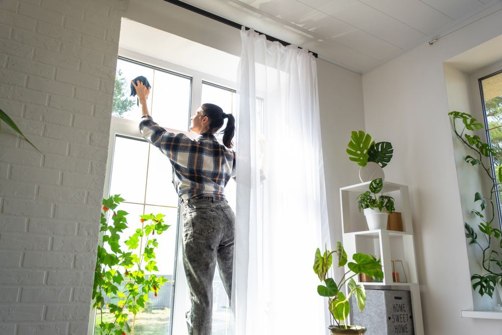 A woman is cleaning a window in a living room.