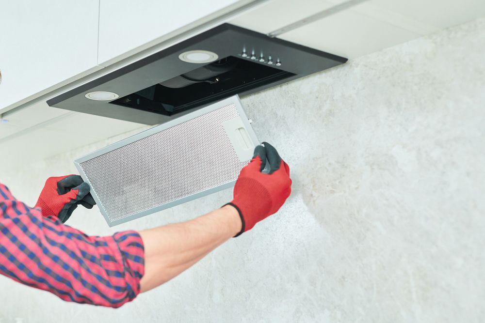 A man is changing the filter on a kitchen hood.