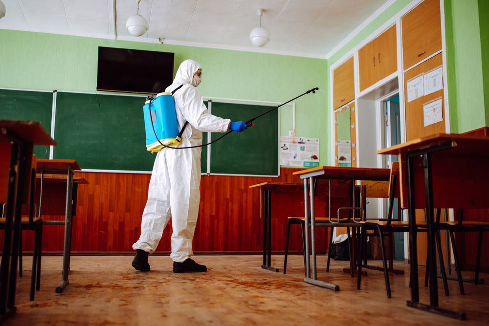 A man in a protective suit is disinfecting a classroom.