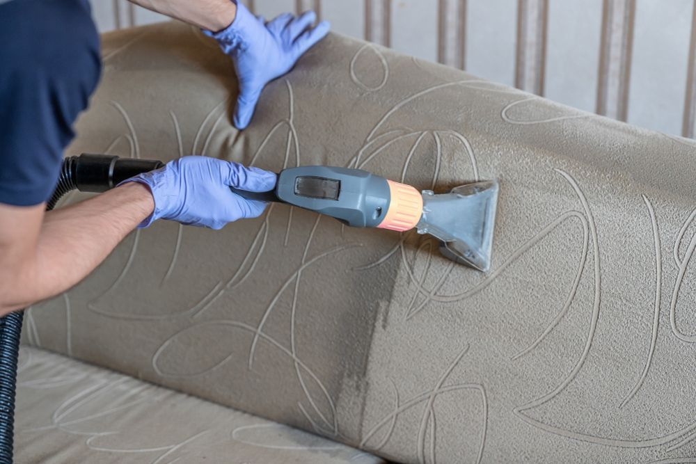 A man is cleaning a couch with a vacuum cleaner.
