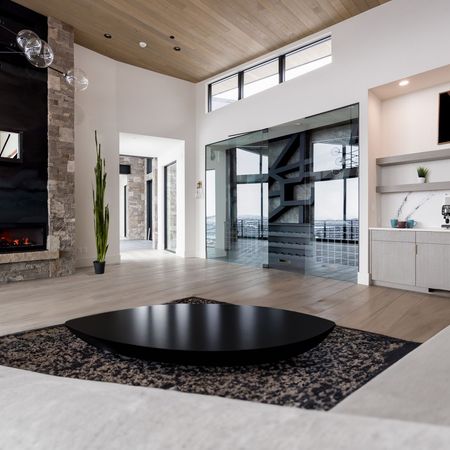 Spacious modern living room with fireplace, black circular table on rug, and large windows.