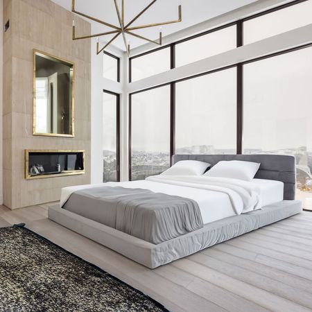 A modern bedroom with a bed near large windows and a fireplace.