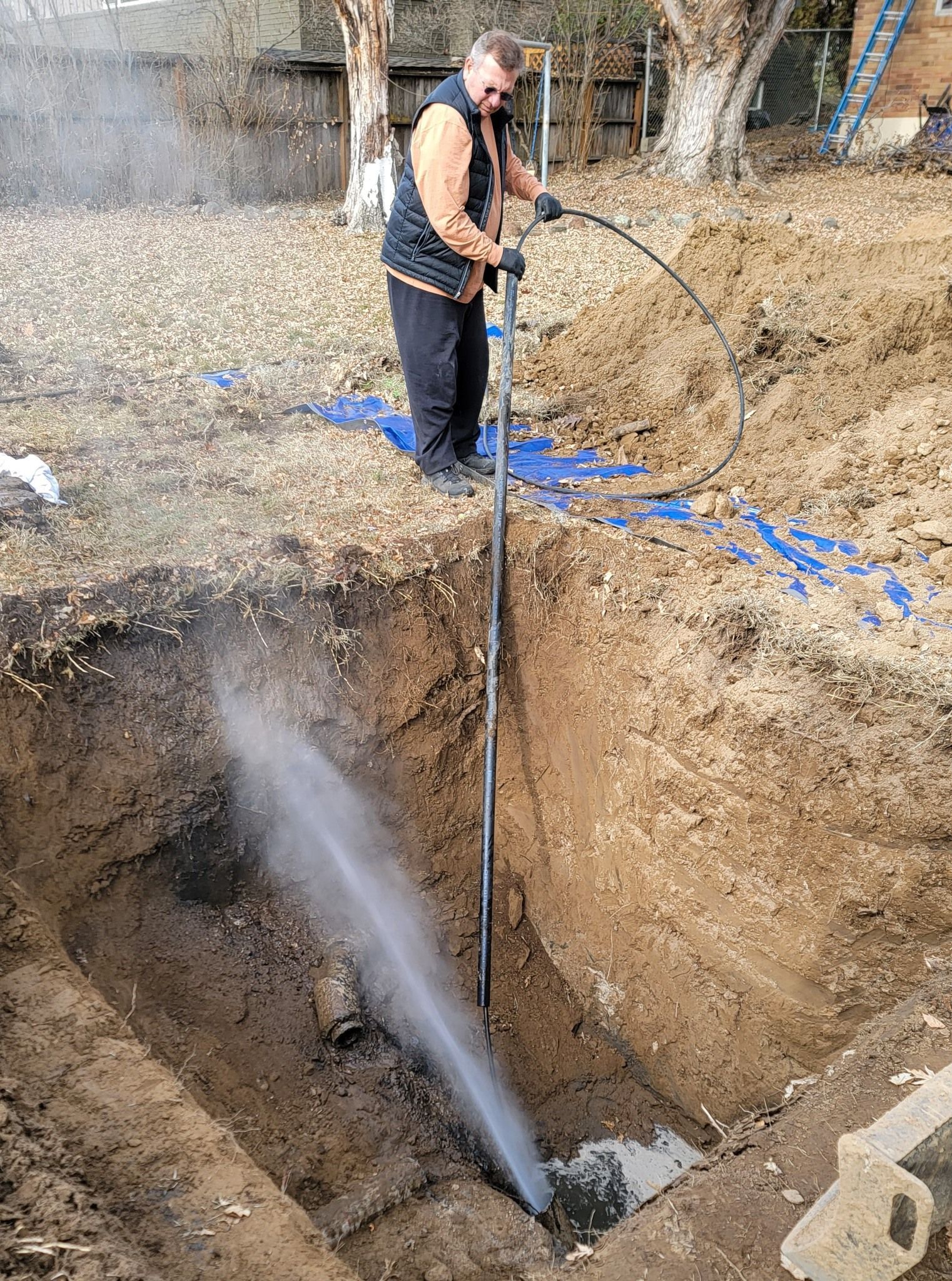 A man is using a high pressure washer to clean a hole in the ground.