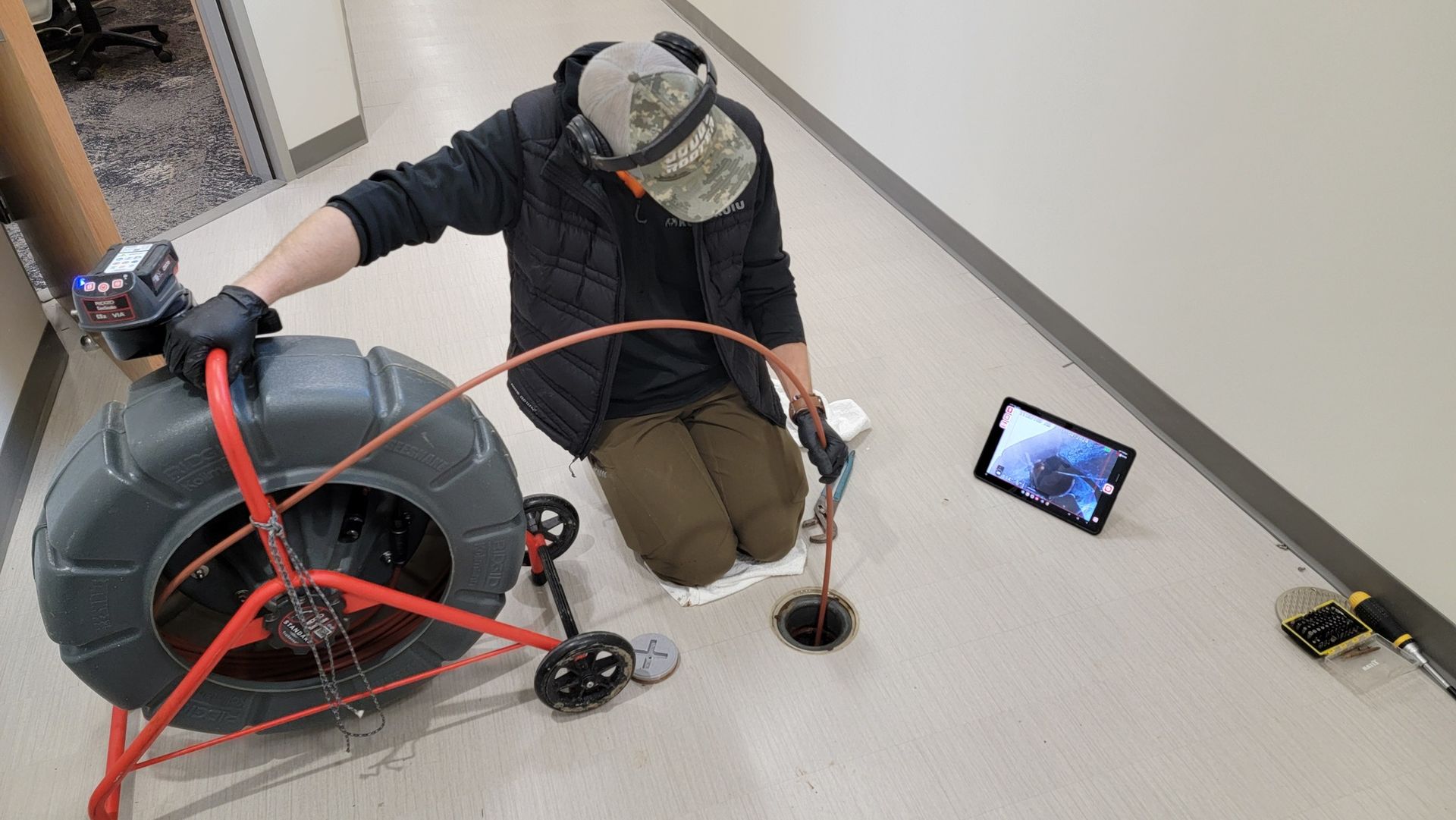 A man is kneeling on the floor using a drain camera.