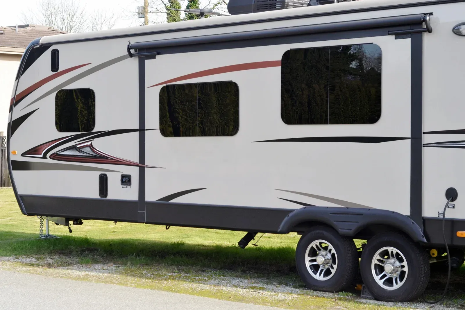 RV parked on grass, featuring three dark-tinted windows, black awning, and dual wheels.