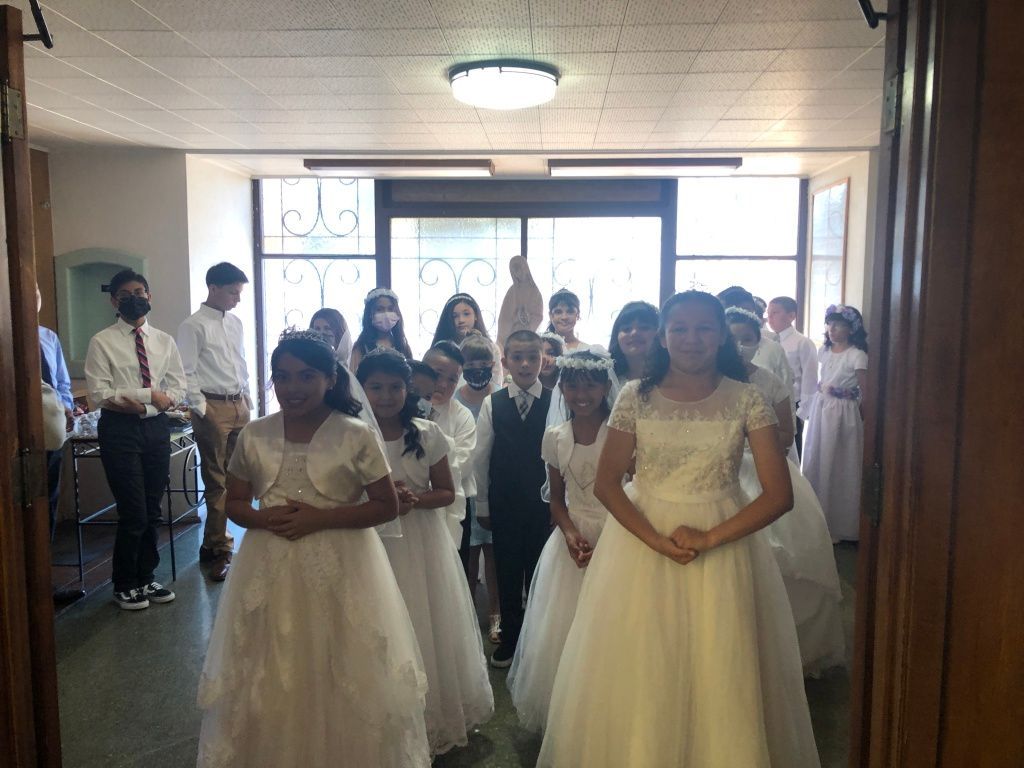 A group of young children in formal attire stands inside a building.