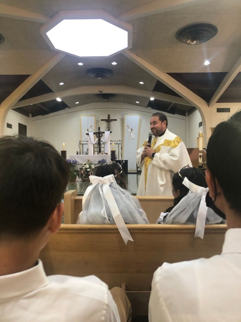 Priest in white and gold robes speaks to a congregation in a church. 