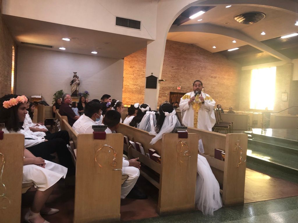 A priest in white and gold robes addresses a congregation during a church ceremony. 