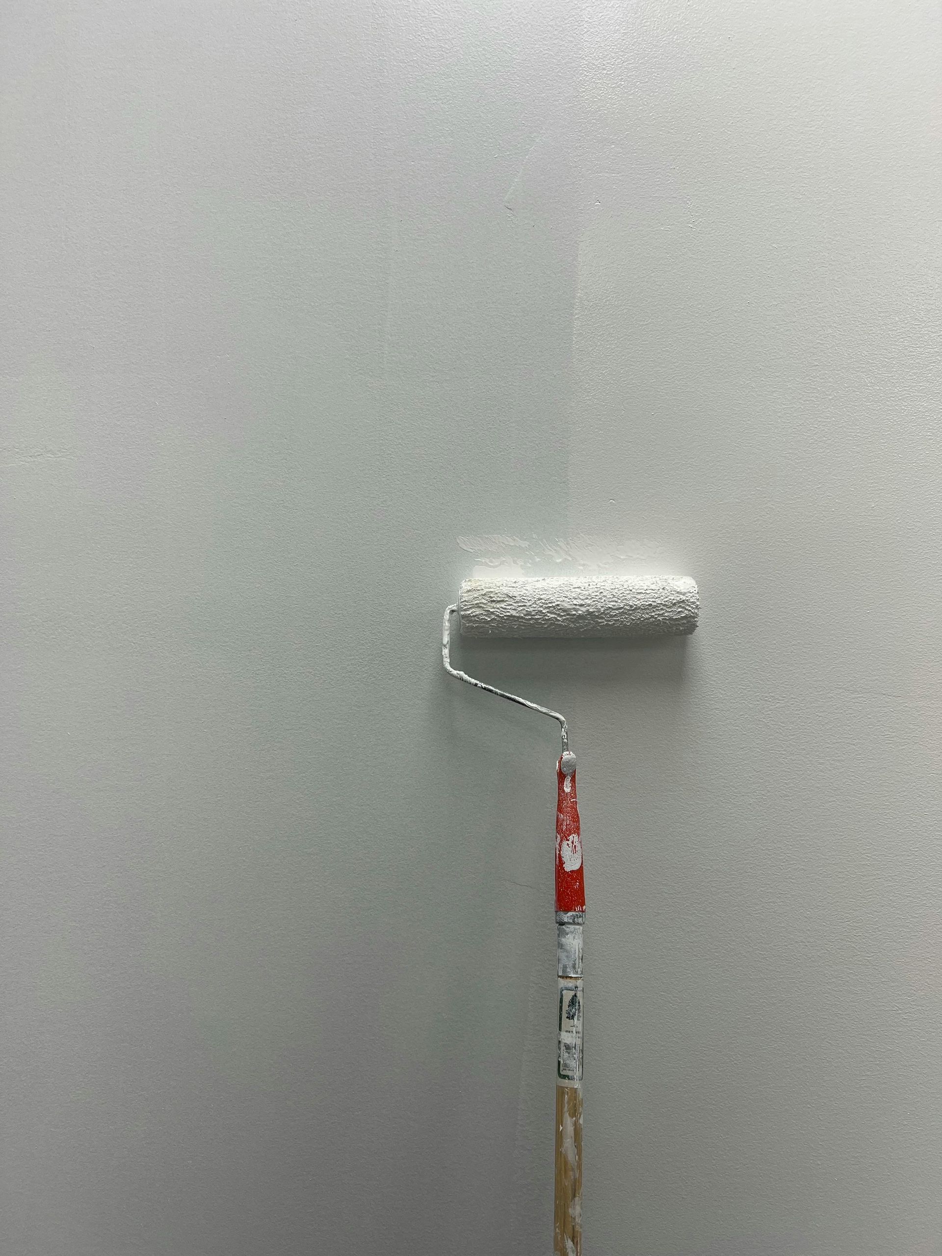 Paint roller applying white paint to a gray wall
