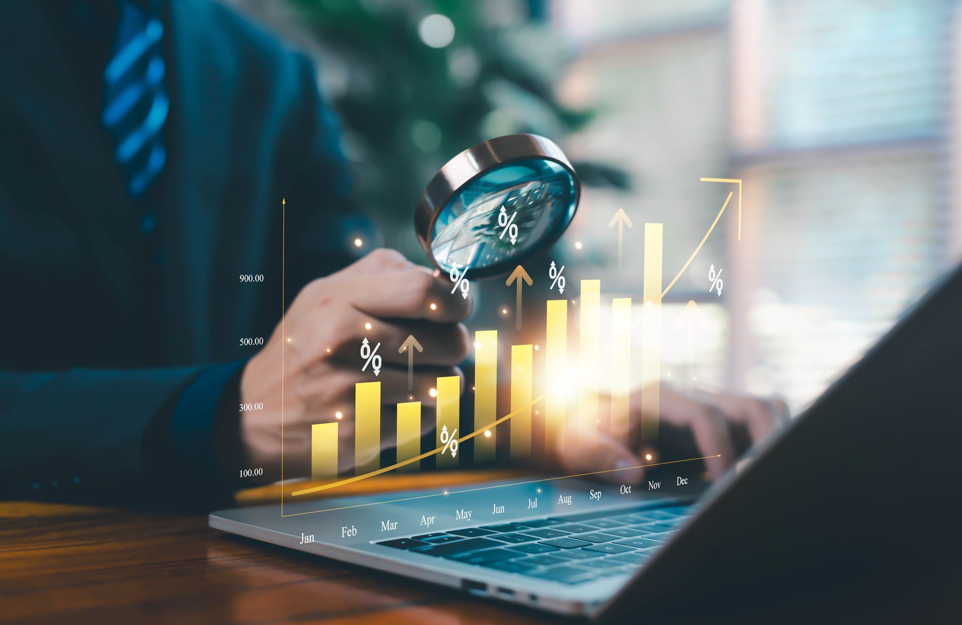 Hand holding magnifying glass over laptop with rising yellow business chart and arrows Hand holding magnifying glass over laptop with rising yellow business chart and arrows