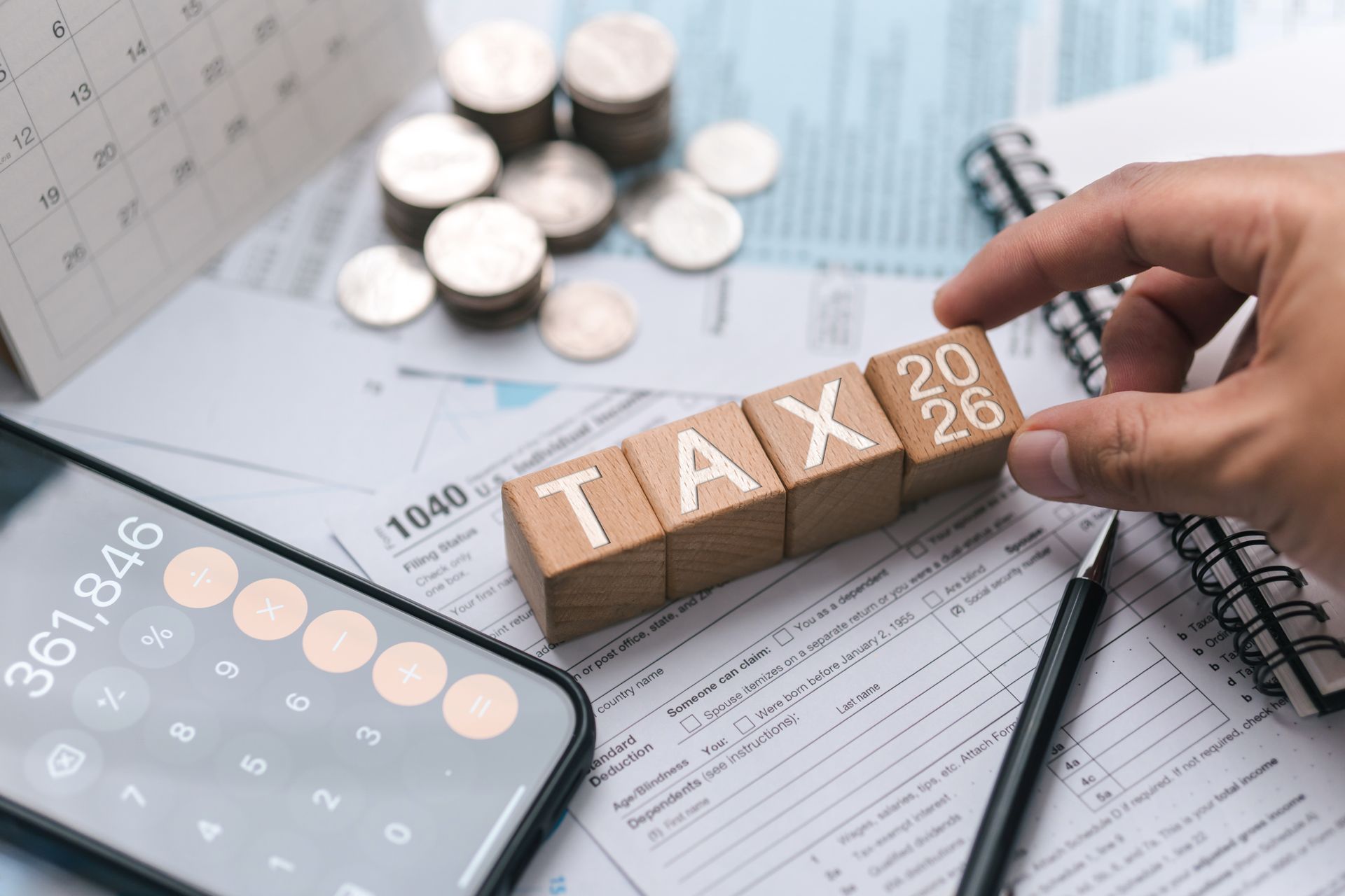 Hand placing TAX blocks on tax forms with calculator and coins, representing tax filing and finance Hand placing TAX blocks on tax forms with calculator and coins, representing tax filing and finance