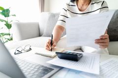 Person reviewing paperwork and writing notes at a bright desk with a laptop and calculator.